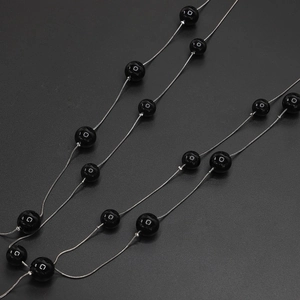 Detail view of black beads on a silver snake chain long necklace and eyewear strap