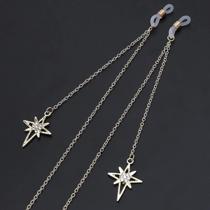 Golden metal eyewear chain with sparkling star pendants on a textured black background