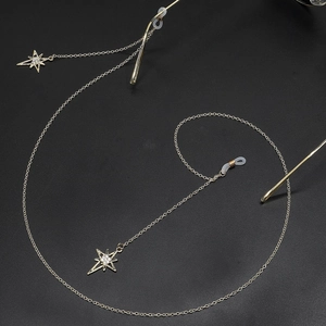 Golden eyewear chain with star charms and crystal details on a black textured background