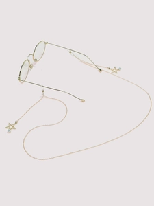 Detail of gold metal eyewear chain with star charms and white pearls on spectacles