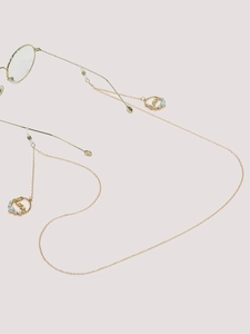 Détail de la chaîne de lunettes dorée avec pendentifs Love et perles sur fond rose