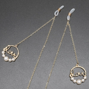 Chaîne à lunettes dorée avec pendentif Love et perles blanches sur fond sombre