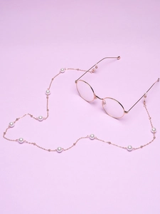 Close-up of rose gold glasses chain with white pearls and silicone ends on purple background