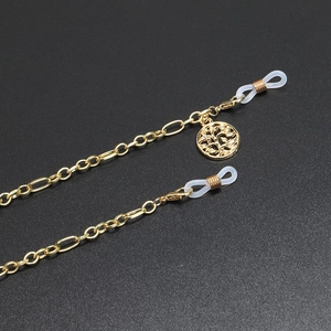 Detail of gold metal glasses chain featuring a Tree of Life pendant on black background
