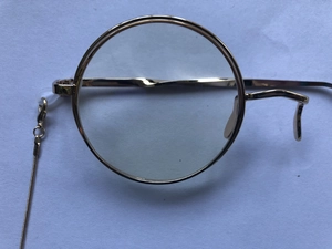 Detail view of a gold-rimmed monocle frame with matching sleek metal snake chain and clasp