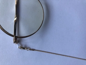 Macro detail of golden round monocle frame with fine snake chain and smooth metallic texture