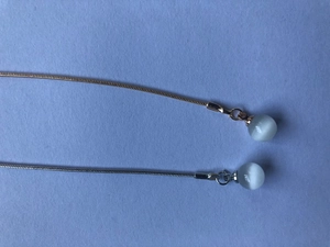 Detail of silver and gold monocle chains with cat eye stone beads on light blue background