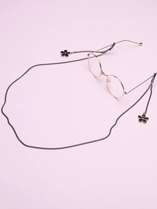 Détail de la chaîne de lunettes dorée avec pendentifs fleurs noires sur fond mauve