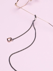 Détail d'une chaîne de lunettes noire avec pendentif cœur ajouré or rose et boucles en silicone