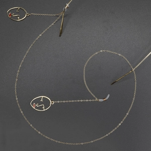 Golden eyewear chain with minimalist face contour charms and red lip accents on dark base