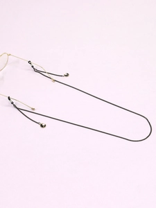 Détail d'une chaîne de lunettes noire avec pendentifs lune dorée sur fond violet clair