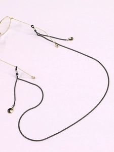 Détail d'une chaîne de lunettes noire avec pendentifs lune et étoile dorés sur fond violet