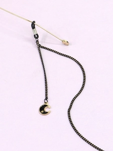 Détail de la chaîne de lunettes noire avec pendentifs étoile et lune dorés sur fond violet