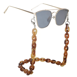 Detail of amber acrylic resin chain strap with gold sunglasses on white background