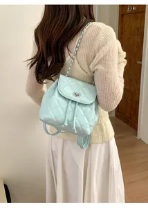 Rear view of model wearing a mint green quilted backpack with silver chain and twist lock