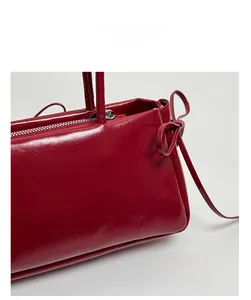 Detail of the elegant wine red leather handbag with a side bow and metallic zipper