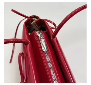 Detail of red patent leather shoulder bag showing shiny silver metal zipper and solid puller