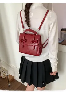 Vista detallada de mochila vintage rojo oscuro con lazos sobre un jersey blanco de moda
