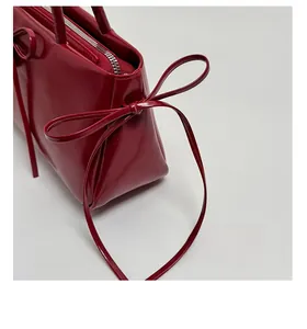 Close-up of deep red glossy underarm bag showing the stylish ribbon knot detail and silver zipper
