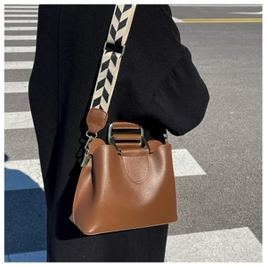 Brown leather bucket bag detail with geometric patterned wide strap and metal handle