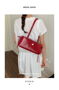 Model wearing a red leather shoulder bag with a bow and heart charm on a white dress