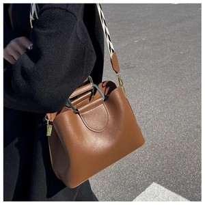 Brown leather bucket bag with geometric strap worn by model on an asphalt road
