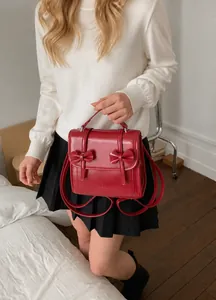 Dettaglio dello zaino in pelle bordeaux lucida con eleganti fiocchi e stile accademico