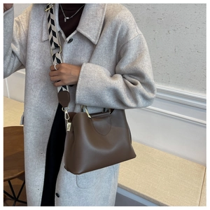Close-up of brown leather bucket bag with patterned wide strap and gold hardware