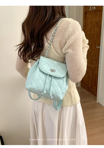 Close-up of light blue quilted backpack with metallic lock and chain strap details