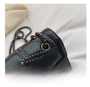 Detail of black leather bag featuring geometric gunmetal studs and chain through eyelets