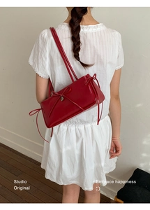 Close-up of a red rectangular shoulder bag with long ribbon bow detail on white dress