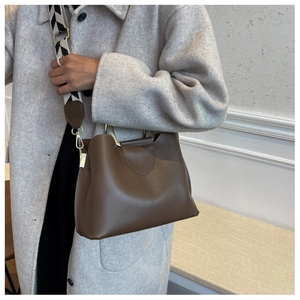 Detail of dark coffee bucket bag with gold circular handle and geometric wide strap