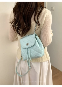 Detail view of mint green quilted backpack with metal lock and chain straps on model
