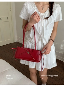 Detail of dark red leather underarm bag with slim bow tie and heart-shaped metal pendant