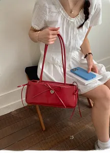 Detail of red faux leather shoulder bag with a bow accent and heart-shaped metal tag