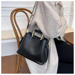 Detail of black leather bucket bag with gold ring handle and geometric wide strap