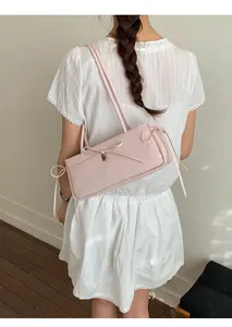 Detailed side view of light pink leather underarm bag with bow and heart pendant