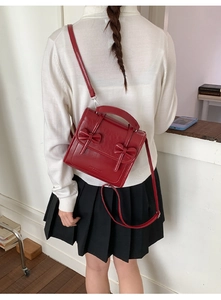 Detalle de bolso bandolera vintage rojo con lazos y correa ajustable mostrado en la modelo