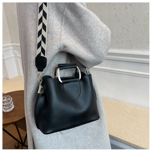 Detail of black leather bucket bag with gold D-handle and geometric woven strap