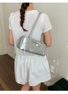 Detail of silver metallic shoulder bag featuring leather bow knots and a heart pendant