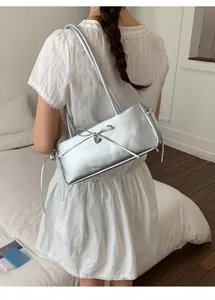 Detail showing elegant silver shoulder bag with bow and heart pendant on white dress
