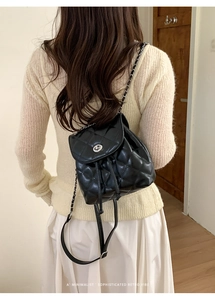 Close-up of minimalist black quilted backpack with silver lock and chain strap detail