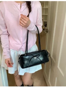 Detail of black glossy shoulder bag with leather bow and silver heart pendant
