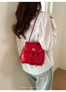 Detail of red quilted backpack featuring silver metallic turn-lock and leather chain strap