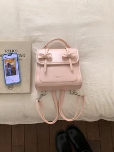 Dettaglio zaino in pelle rosa con fiocchi e logo in rilievo su sfondo di tessuto bianco