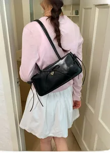 Detail of black bow shoulder bag with silver heart pendant worn by model in light room