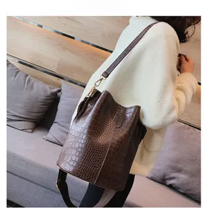 Detail of dark brown faux crocodile leather bucket bag worn by model on shoulder
