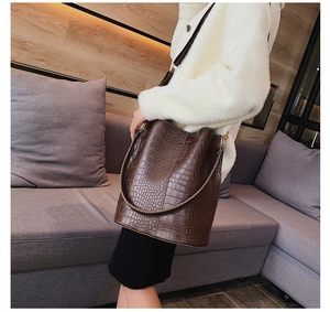 Detail of dark brown crocodile pattern bucket bag with gold hardware worn by model
