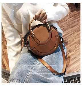 Borsa tonda marrone in pelle con manico ad anello dorato e borchie, vista su modella