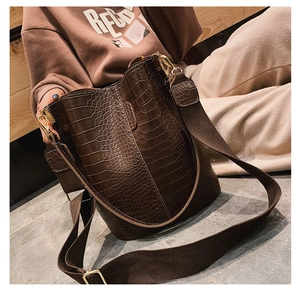 Detail of dark brown crocodile embossed bucket bag with wide fabric strap and gold hardware